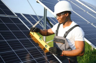 Güvenlik kaskı ve üniforma takan Afro-Amerikan elektrik mühendisinin portresi güneş panelleri kuruyor.