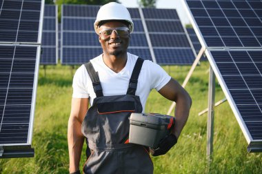 Güvenlik kaskı ve üniforma takan Afro-Amerikan elektrik mühendisinin portresi güneş panelleri kuruyor.