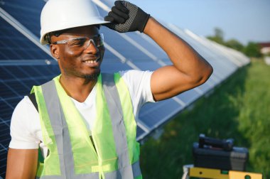Güvenlik kaskı ve üniforma takan Afro-Amerikan elektrik mühendisinin portresi güneş panelleri kuruyor.