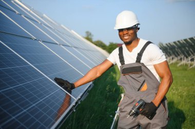 Güneş pili panellerini koruyan Afrikalı Amerikalı mühendis. Ekolojik güneş çiftliği inşaatında çalışan bir teknisyen. Yenilenebilir temiz enerji teknolojisi kavramı.
