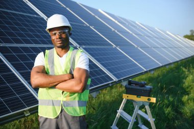 Güneş pili panellerini koruyan Afrikalı Amerikalı mühendis. Ekolojik güneş çiftliği inşaatında çalışan bir teknisyen. Yenilenebilir temiz enerji teknolojisi kavramı.