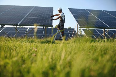 Güvenlik kaskı ve gözlüklü Afrikalı Amerikalı adam güneş panellerini tornavidayla sıkıyor. İstasyonda servis çalışması yaparken araçları kullanan yetkili teknisyen.