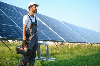 Üniformalı ve aletleri olan Hintli bir işçi güneş paneli çiftliğinde çalışıyor..
