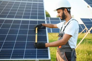 Güneş paneli yakınında çalışan üniformalı Hintli adam.