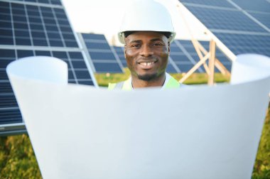 Afrikalı Amerikalı teknisyen güneş panellerinin bakımını kontrol ediyor. Güneş istasyonundaki siyah adam mühendisi.