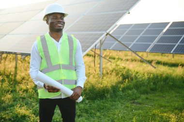 Afrikalı Amerikalı teknisyen güneş panellerinin bakımını kontrol ediyor. Güneş istasyonundaki siyah adam mühendisi.