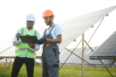 Güvenlik kasklı çok ırklı bir grup insan güneş istasyonunda duruyor ve ellerinde büyük çizimler olan kameralara bakıyor. İki mühendis ve teknisyen dışarıdaki panelleri inceliyor..