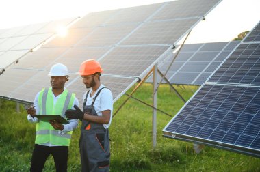 Güneş panellerindeki çok ırklı mühendisler. Afrika kökenli Amerikalı ve Arap mühendis güneş paneli çiftliğinde çalışıyor.