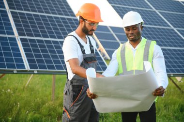 Güneş panellerindeki çok ırklı mühendisler. Afrika kökenli Amerikalı ve Arap mühendis güneş paneli çiftliğinde çalışıyor.