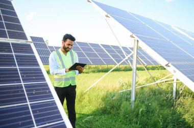 Yeşil yelekli Hintli bir erkek mühendis güneş panelleri üzerinde çalışıyor. Yenilenebilir enerji kavramı