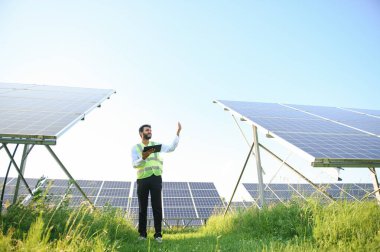 Genç Hintli erkek mühendisin portresi güneş panellerinin yanında duruyor, açık mavi gökyüzü arka planı, yenilenebilir ve temiz enerjisi var. beceri Hindistan, kopyalama alanı