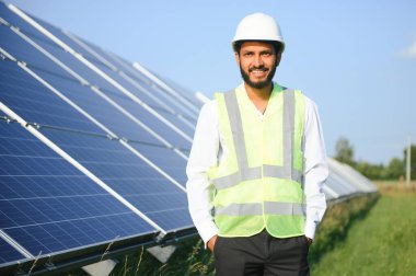 Genç Hintli erkek mühendisin portresi güneş panellerinin yanında duruyor, açık mavi gökyüzü arka planı, yenilenebilir ve temiz enerjisi var. beceri Hindistan, kopyalama alanı