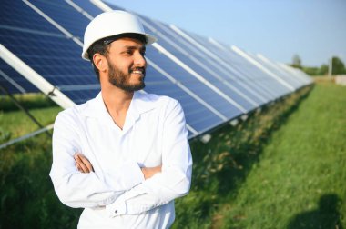 Genç Hintli erkek mühendisin portresi güneş panellerinin yanında duruyor, açık mavi gökyüzü arka planı, yenilenebilir ve temiz enerjisi var. beceri Hindistan, kopyalama alanı