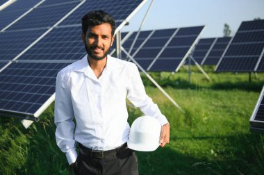 Genç Hintli teknisyen ya da yönetici güneş panelinin yanında duran resmi giysiler giyiyor. Yenilenebilir enerji, çapraz duran adam, boşluğu kopyala.