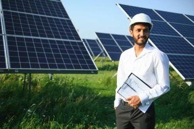 Yeşil yelekli Hintli bir erkek mühendis güneş panelleri üzerinde çalışıyor. Yenilenebilir enerji kavramı