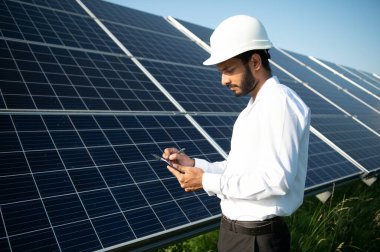 Genç Hintli erkek mühendisin portresi güneş panellerinin yanında duruyor, açık mavi gökyüzü arka planı, yenilenebilir ve temiz enerjisi var. beceri Hindistan, kopyalama alanı