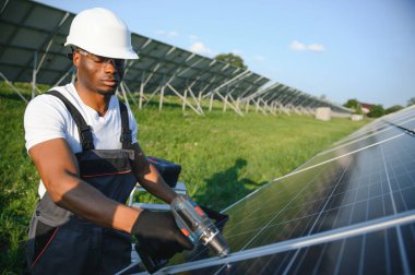 Güvenlik kaskı ve üniforma takan Afro-Amerikan elektrik mühendisinin portresi güneş panelleri kuruyor.