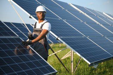 Güvenlik kaskı ve üniforma takan Afro-Amerikan elektrik mühendisinin portresi güneş panelleri kuruyor.