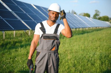 Güvenlik kaskı ve üniforma takan Afro-Amerikan elektrik mühendisinin portresi güneş panelleri kuruyor.