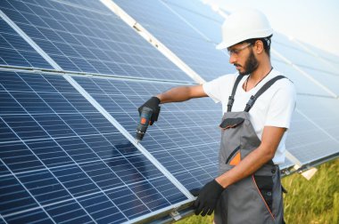 Üniformalı ve aletleri olan Hintli bir işçi güneş paneli çiftliğinde çalışıyor..