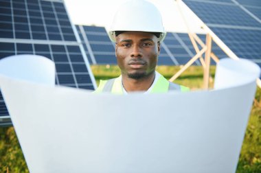 Genç, yakışıklı Afrikalı Amerikalı zanaatkârın yakın portresi koruyucu bir miğfer. Tulumlu, kameraya gülümseyen mutlu bir adam. Yavaş çekim