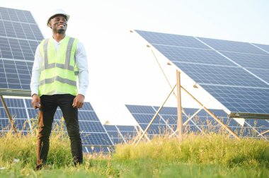 Afrikalı Amerikalı teknisyen güneş panellerinin bakımını kontrol ediyor. Güneş istasyonundaki siyah adam mühendisi.