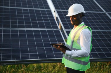 Afrikalı Amerikalı teknisyen güneş panellerinin bakımını kontrol ediyor. Güneş istasyonundaki siyah adam mühendisi.