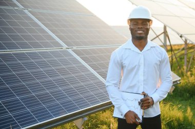 Afrikalı Amerikalı teknisyen güneş panellerinin bakımını kontrol ediyor. Güneş istasyonundaki siyah adam mühendisi.