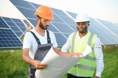 Güneş panellerindeki çok ırklı mühendisler. Afrika kökenli Amerikalı ve Arap mühendis güneş paneli çiftliğinde çalışıyor.