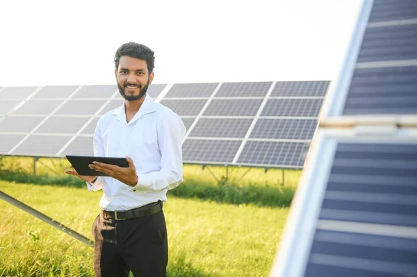 male engineer checks a photovoltaic (solar) plant and uses a recording tablet. Indian Man in uniform holding tablet
