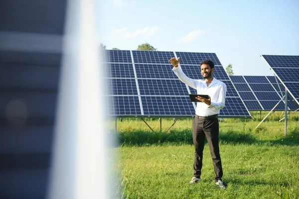 Güneş panellerinin yanında duran tabletli genç erkek mühendis, temiz mavi gökyüzü geçmişe sahip tarım arazisi, yenilenebilir enerji, temiz enerji