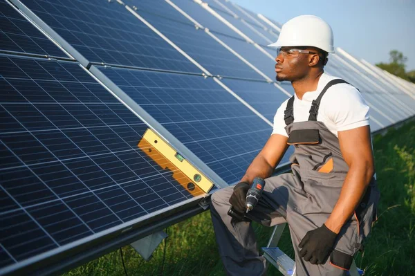 Güvenlik kaskı ve üniforma takan Afro-Amerikan elektrik mühendisinin portresi güneş panelleri kuruyor.