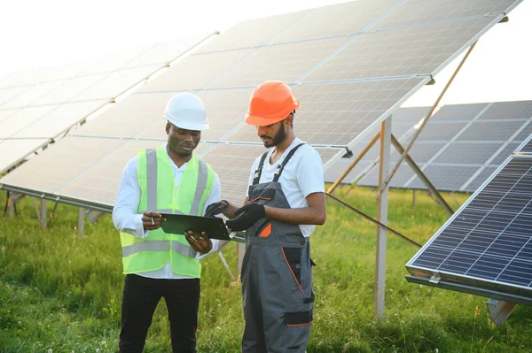 Güvenlik kasklı çok ırklı bir grup insan güneş istasyonunda duruyor ve ellerinde büyük çizimler olan kameralara bakıyor. İki mühendis ve teknisyen dışarıdaki panelleri inceliyor..