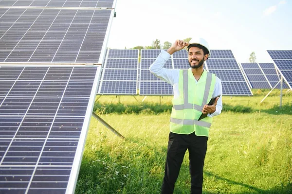 Genç Hintli teknisyen ya da yönetici güneş panelinin yanında duran resmi giysiler giyiyor. Yenilenebilir enerji, çapraz duran adam, boşluğu kopyala.