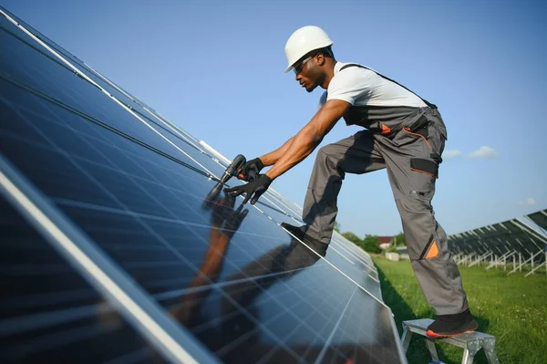 Portrait of african american electrician engineer in safety helmet and uniform installing solar panels