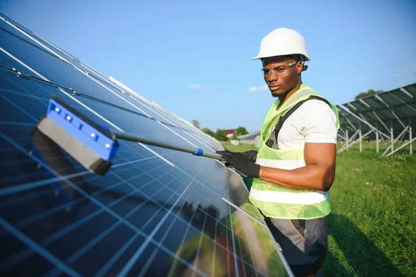 Güneş enerjisi santralinde güneş panelini temizleyen Afrikalı Amerikan işçisi.