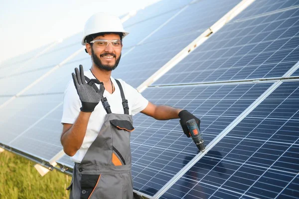 Kasklı ve kahverengi tulumlu erkek Arap mühendis güneş panellerindeki direnci kontrol ediyor. İstasyonda çalışan Hintli adam.