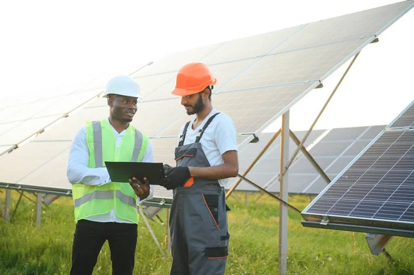 Güneş panellerindeki çok ırklı mühendisler. Afrika kökenli Amerikalı ve Arap mühendis güneş paneli çiftliğinde çalışıyor.