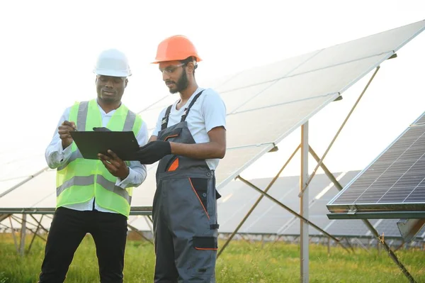 Güvenlik kasklı çok ırklı bir grup insan güneş istasyonunda duruyor ve ellerinde büyük çizimler olan kameralara bakıyor. İki mühendis ve teknisyen dışarıdaki panelleri inceliyor..