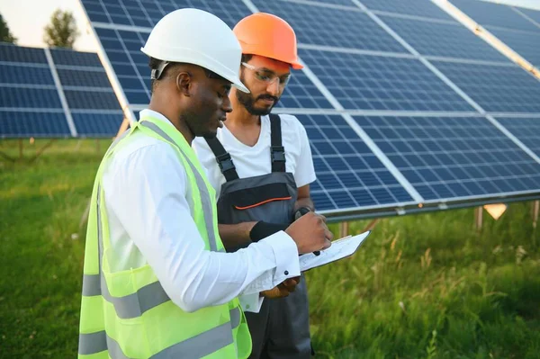 Güvenlik kasklı çok ırklı bir grup insan güneş istasyonunda duruyor ve ellerinde büyük çizimler olan kameralara bakıyor. İki mühendis ve teknisyen dışarıdaki panelleri inceliyor..