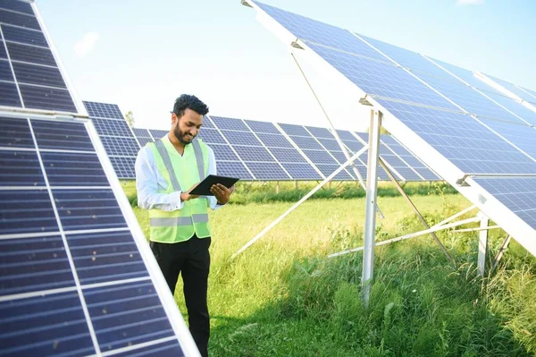 Yeşil yelekli Hintli bir erkek mühendis güneş panelleri üzerinde çalışıyor. Yenilenebilir enerji kavramı