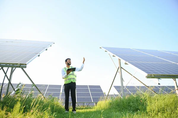 Genç Hintli erkek mühendisin portresi güneş panellerinin yanında duruyor, açık mavi gökyüzü arka planı, yenilenebilir ve temiz enerjisi var. beceri Hindistan, kopyalama alanı