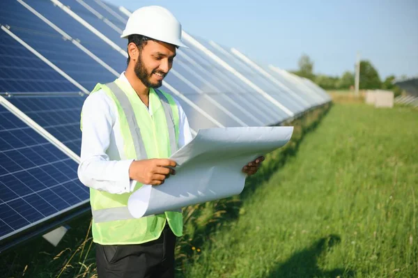 Genç Hintli teknisyen ya da yönetici güneş panelinin yanında duran resmi giysiler giyiyor. Yenilenebilir enerji, çapraz duran adam, boşluğu kopyala.