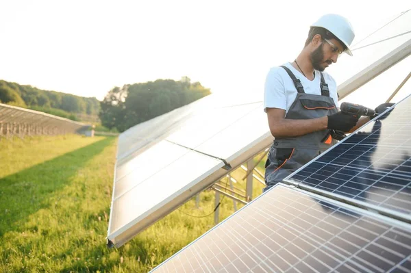 Kasklı ve kahverengi tulumlu erkek Arap mühendis güneş panellerindeki direnci kontrol ediyor. İstasyonda çalışan Hintli adam.