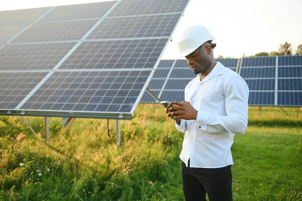 Beyaz gömlekli ve şapkalı Afro-Amerikalı bir mühendis güneş panelleri üzerinde çalışıyor. Güneş enerjisi yenilenebilir enerji kavramı