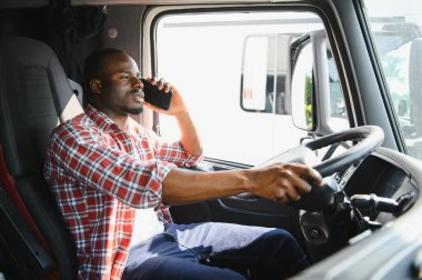 Bir kamyonun kabinindeki Afrikalı sürücü telefonla konuşuyor.