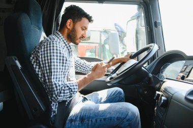 Genç, yakışıklı Hintli adam kamyonunda akıllı telefon kullanıyor.