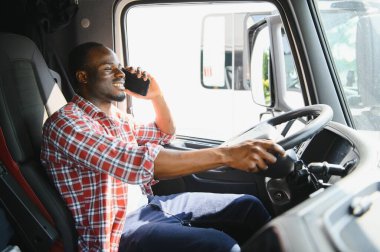 Bir kamyonun kabinindeki Afrikalı sürücü telefonla konuşuyor.
