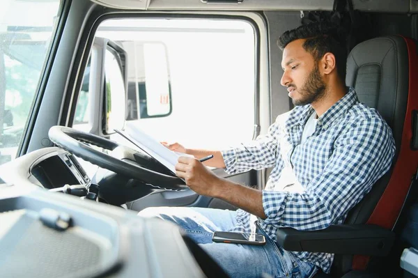 配達倉庫の駐車場に立っている間郵送物リストを点検するインドのトラックの運転者 ロイヤリティフリーのストック画像
