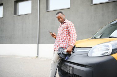 Afrika kökenli Amerikalı bir adam araç şarj istasyonunda araba şarj ediyor..